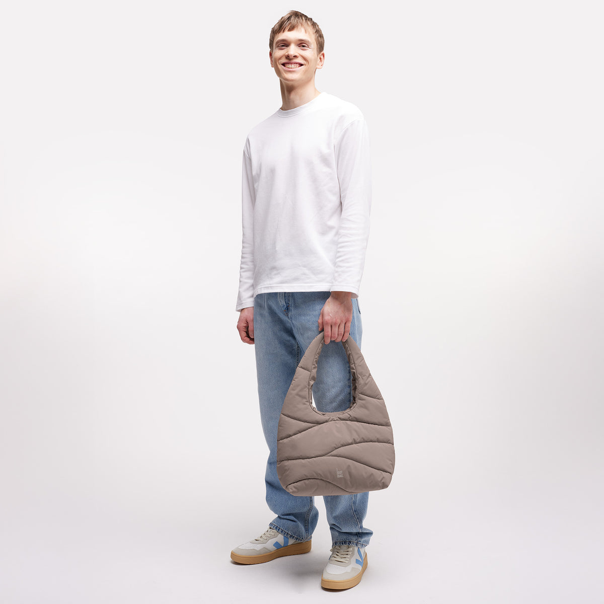 WAVY PUFFER SHOULDER BAG Tasche in oyster (klassisches Taupe-Braun) von einem Mann in der Hand gehalten.