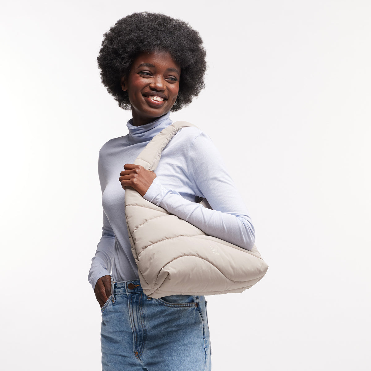 WAVY PUFFER SHOULDER BAG Tasche in scallop (helles Beige) von einer Frau über der Schulter getragen.
