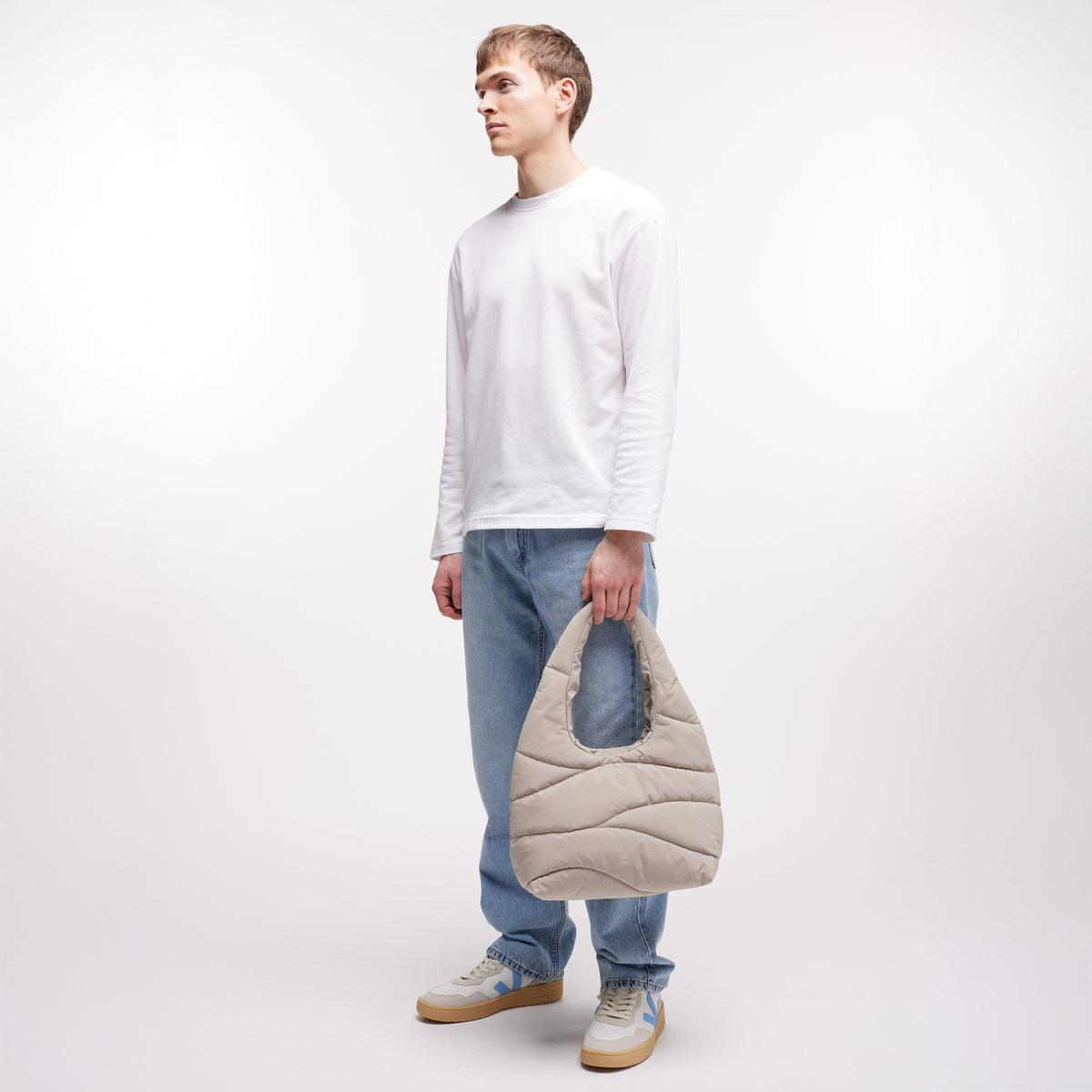 WAVY PUFFER SHOULDER BAG Tasche in scallop (helles Beige) von einem Mann in der Hand gehalten.