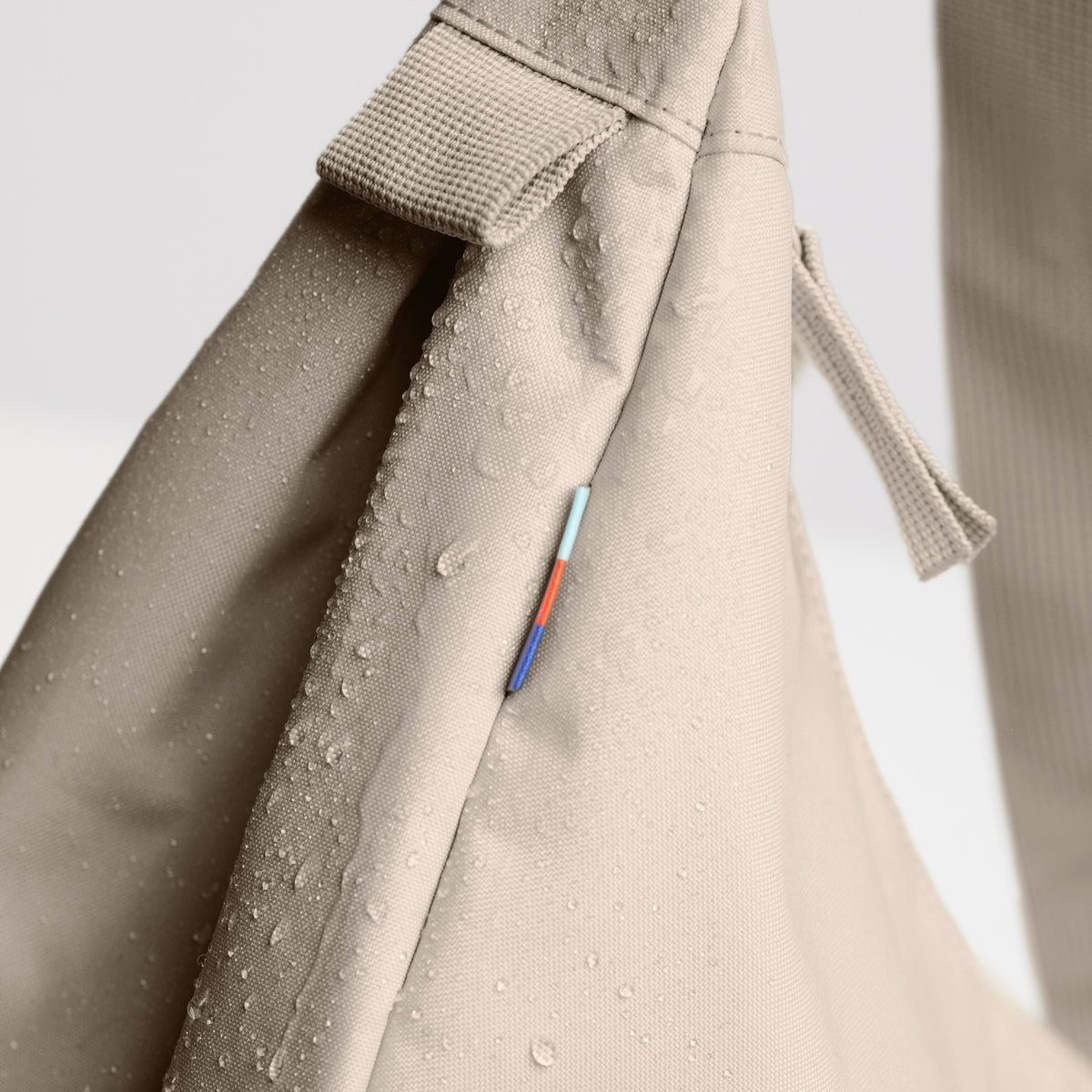 MOON BAG LARGE Tasche in scallop (helles Beige) Detailaufnahme mit Wassertropfen und farbigem Label.