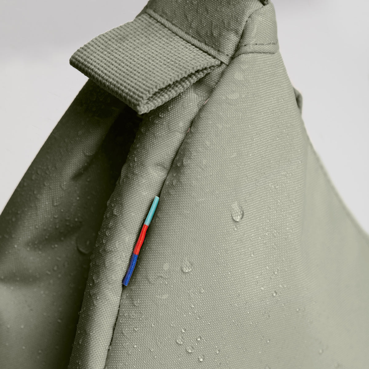 MOON BAG SMALL Tasche in seabed (helles Olivgrün) als Detailaufnahme mit Wassertropfen und kleinem bunten Etikett.
