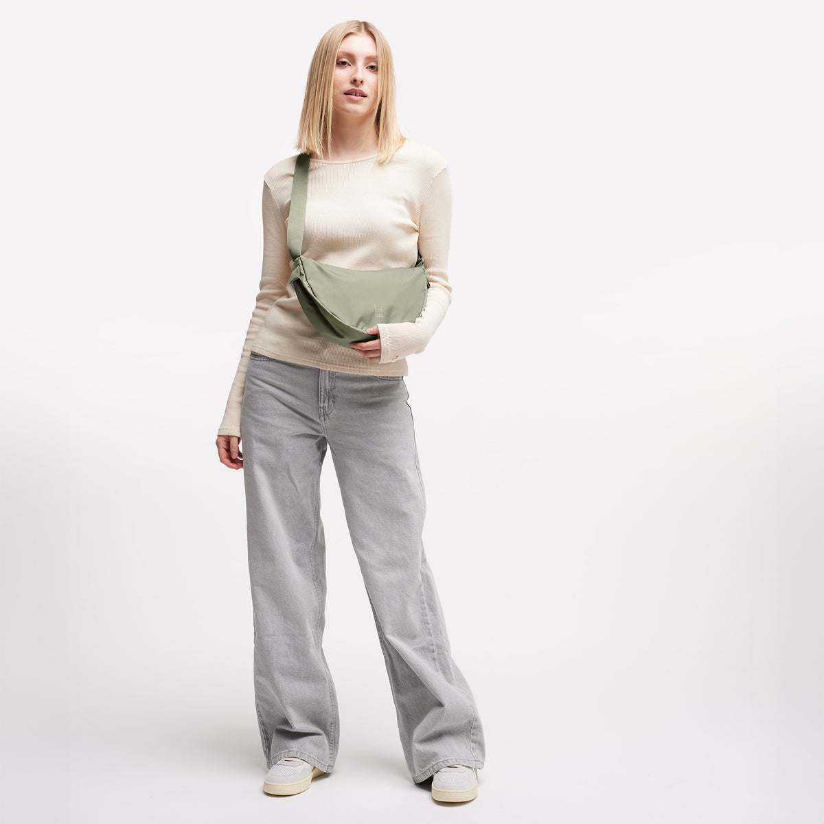 MOON BAG SMALL Tasche in seabed (helles Olivgrün) von einer Frau crossbody getragen.