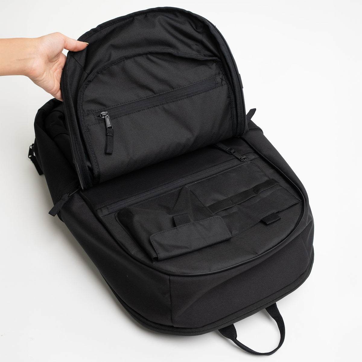 HYBRID PACK Rucksack in black (Schwarz), geöffnet von einer Hand, zeigt Innentaschen.