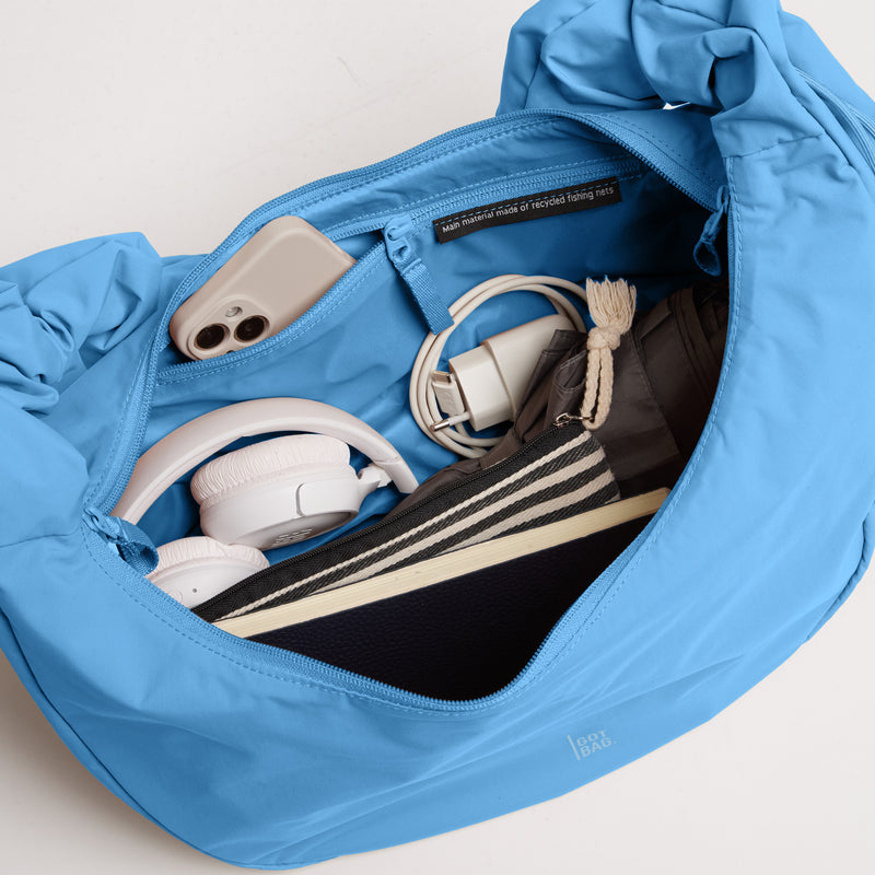 MOON BAG RUFFLE Tasche in aqua (leuchtendes Hellblau) als Detailaufnahme des geöffneten Innenbereichs mit Inhalt.