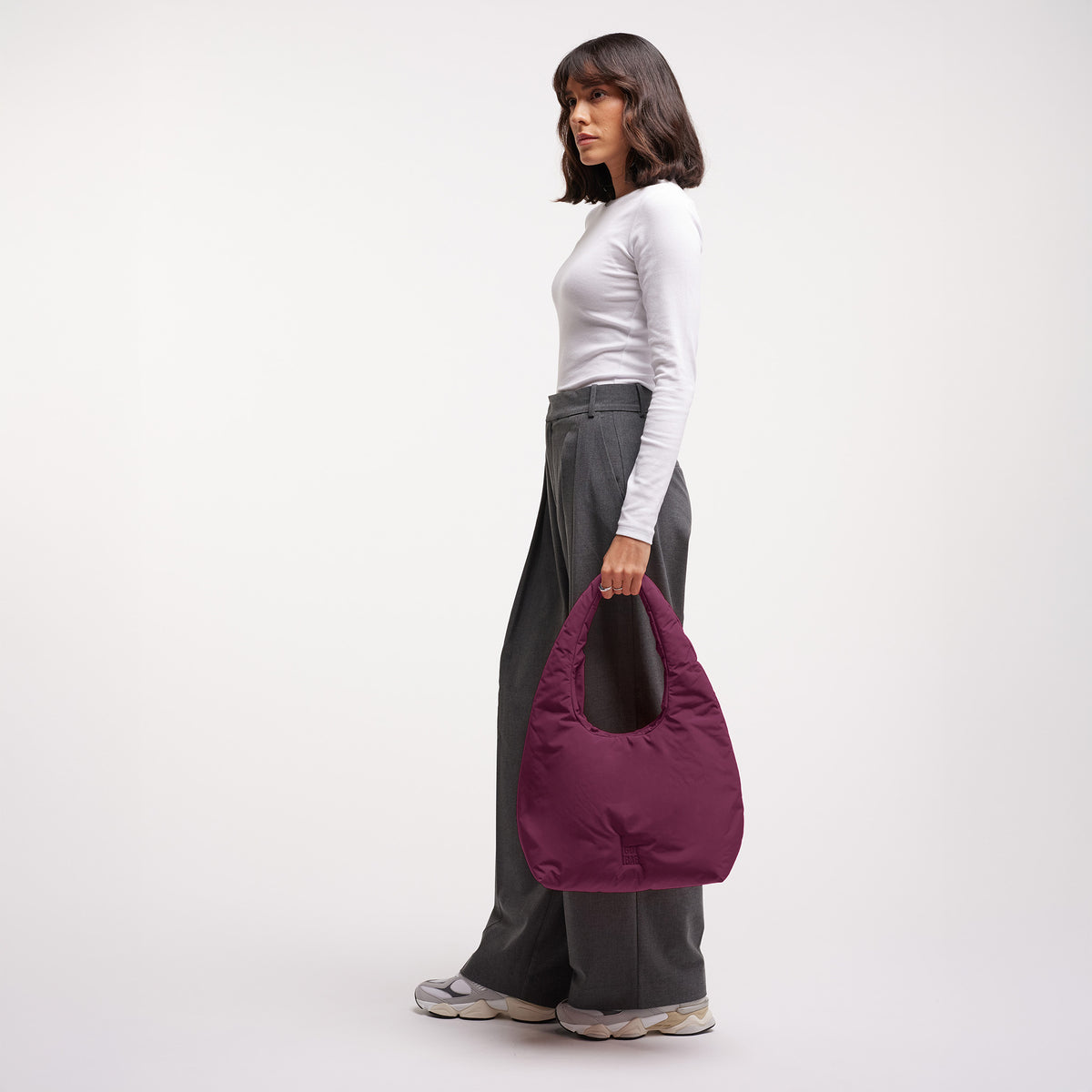 CLOUD SHOULDER BAG Tasche in kraken (Weinrot) von einer Frau in der Hand gehalten.