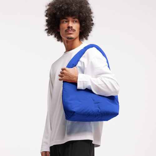 CLOUD SHOULDER Tasche in cobalt (leuchtendes Kobaltblau) von einem Mann über der Schulter getragen.
