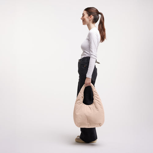 CLOUD SHOULDER Tasche in pearl (helles Puder-Rosa) von einer Frau in der Hand gehalten.
