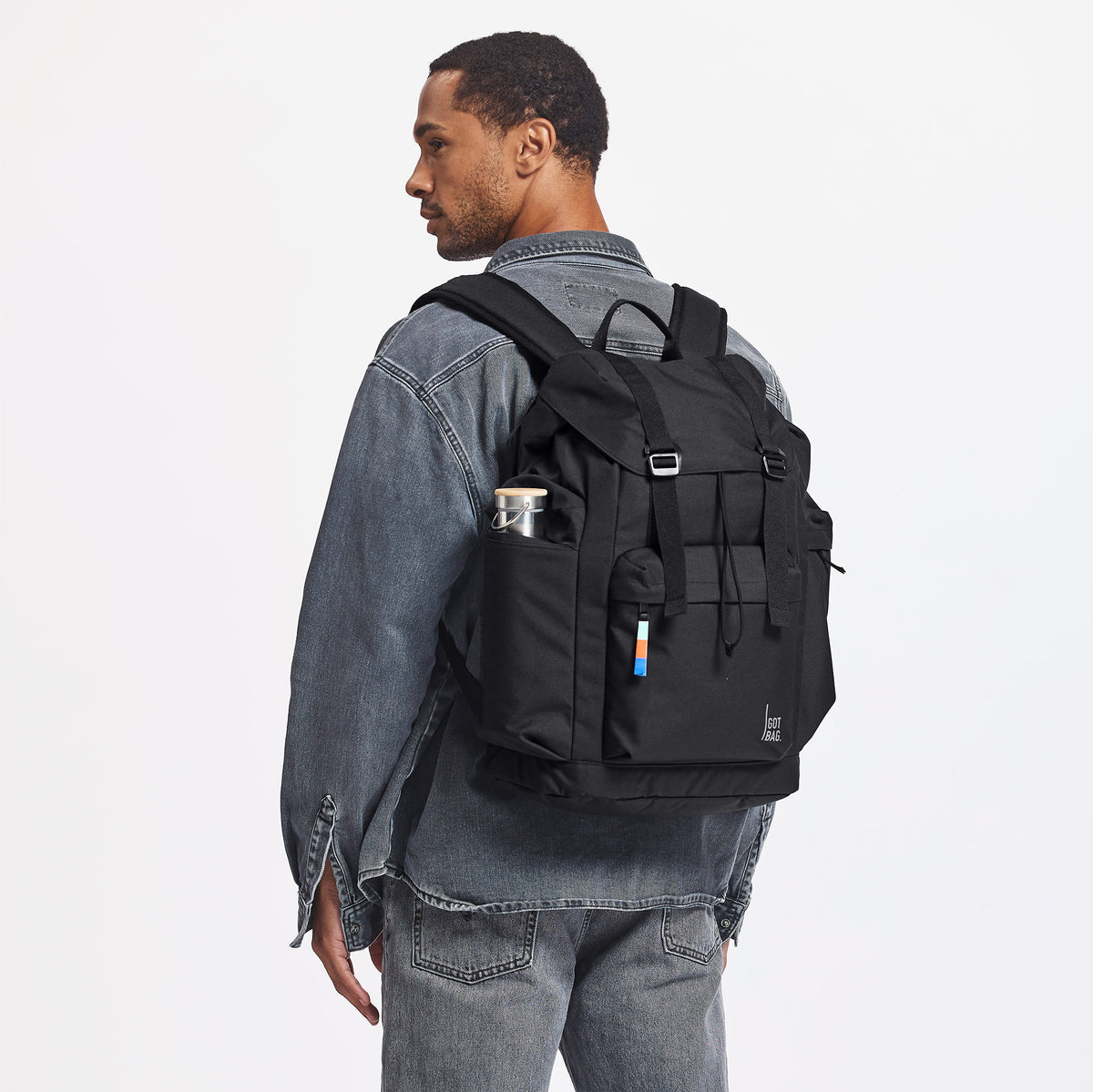 FLAP PACK LARGE Rucksack in black (Schwarz) von einem Mann als Rucksack auf dem Rücken getragen.