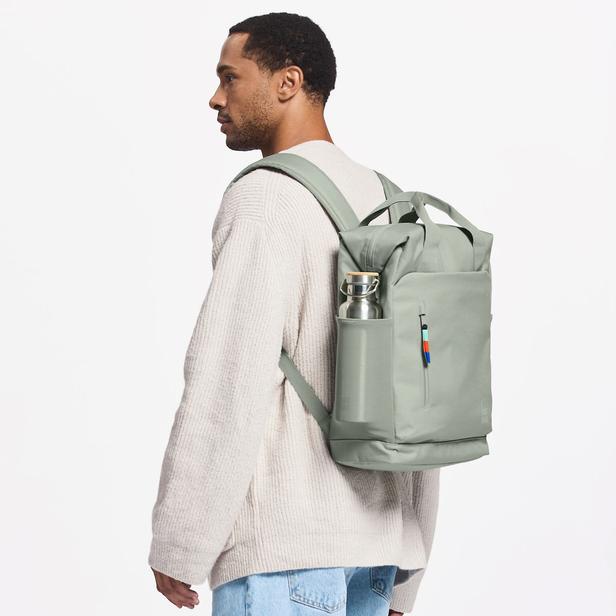 FLOW PACK Rucksack in bass (Salbeigrün) von einem Mann auf dem Rücken getragen.
