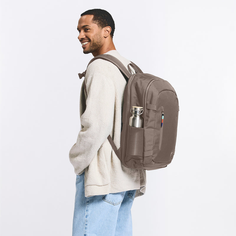 HYBRID PACK Rucksack in oyster (klassisches Taupe-Braun) von einem Mann auf dem Rücken getragen, mit Trinkflasche.