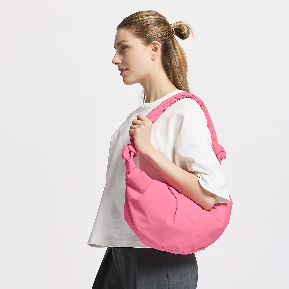 PLEAT MOON BAG LARGE Tasche in salina pink (leuchtendes Pink) von einer Frau über der Schulter getragen.
