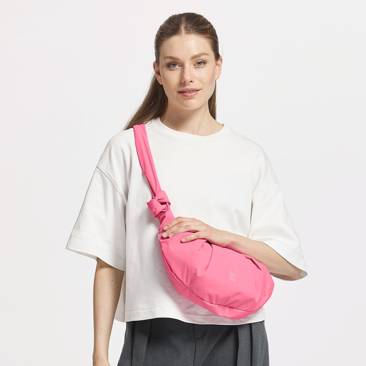 PLEAT MOON BAG SMALL Tasche in salina pink (leuchtendes Pink) von einer Frau crossbody getragen.