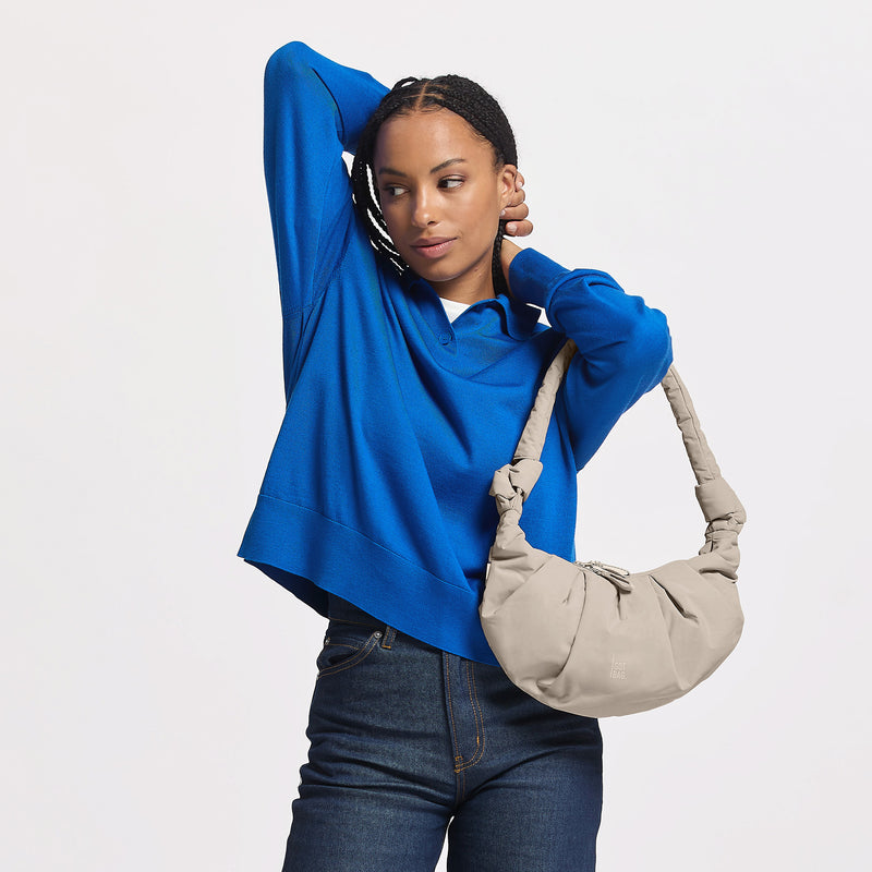 PLEAT MOON BAG SMALL Tasche in soft shell (warmes Cremeweiß) von einer Frau über der Schulter getragen.