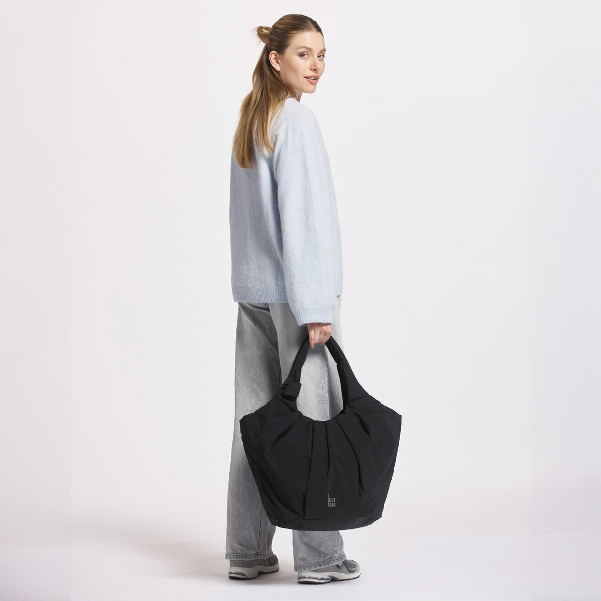 PLEAT TOTE BAG Tasche in black (Schwarz) von einer Frau in der Hand gehalten.