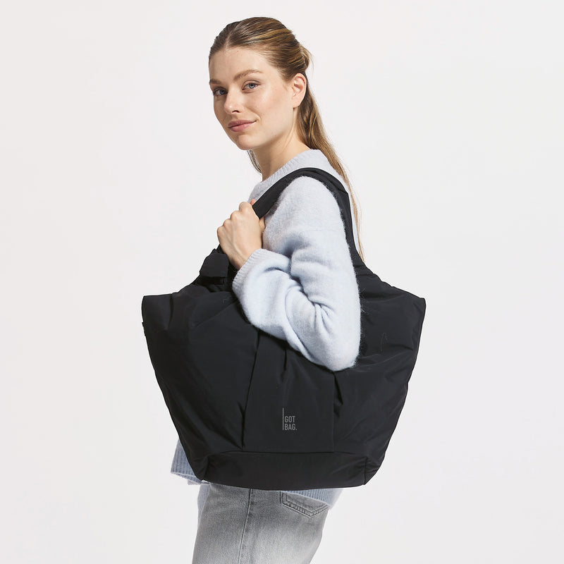 PLEAT TOTE BAG Tasche in black (Schwarz) von einer Frau über der Schulter getragen.