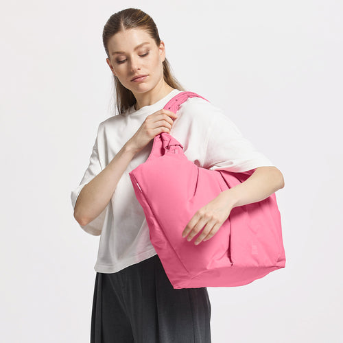 PLEAT TOTE BAG Tasche in salina pink (leuchtendes Pink) von einer Frau über der Schulter getragen.