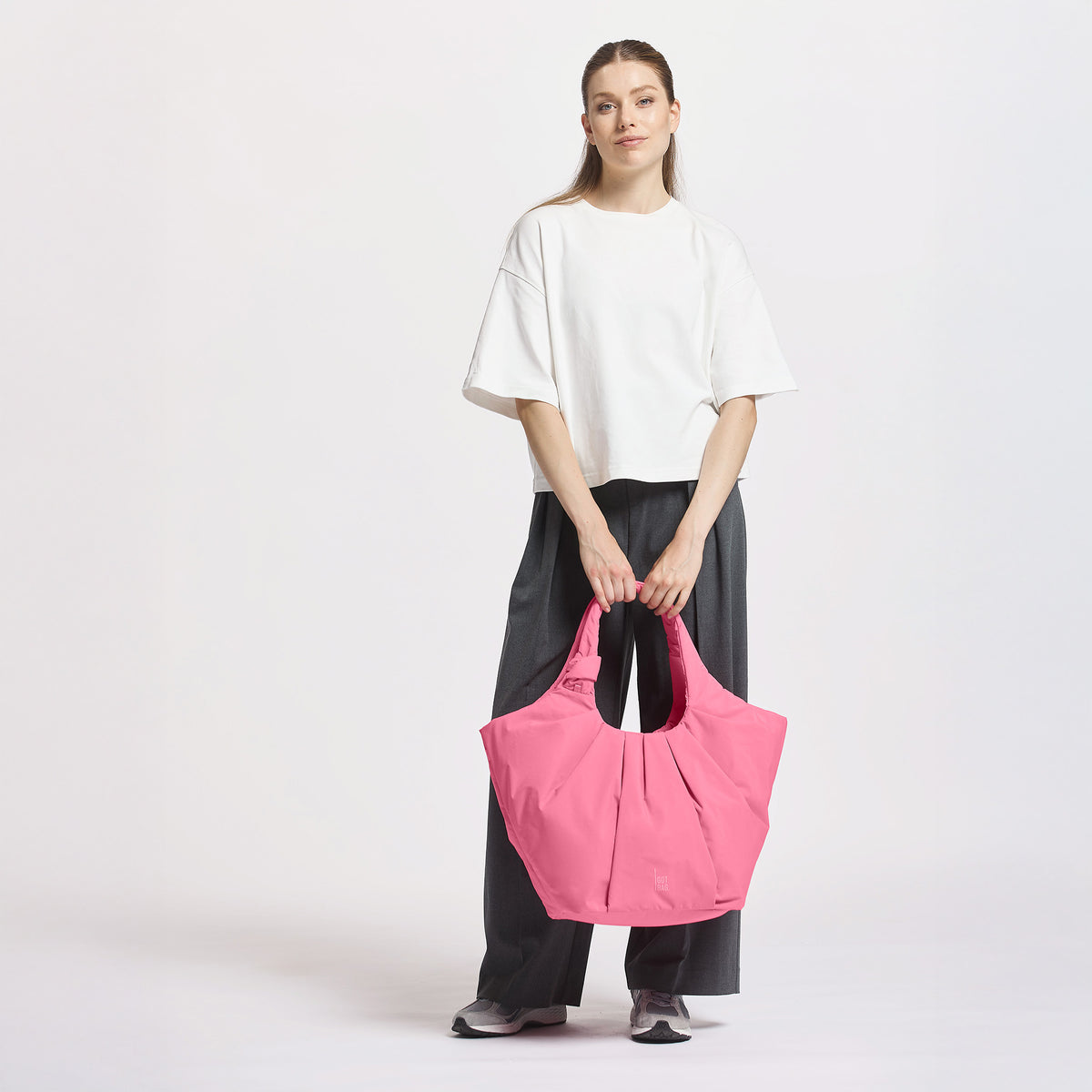 PLEAT TOTE BAG Tasche in salina pink (leuchtendes Pink) von einer Frau in der Hand gehalten.