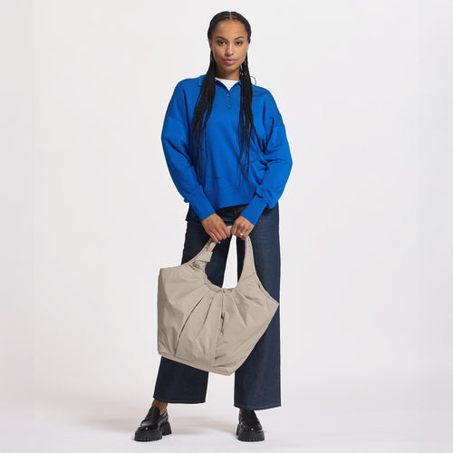 PLEAT TOTE BAG Tasche in scallop (helles Beige) von einer Frau in der Hand gehalten.