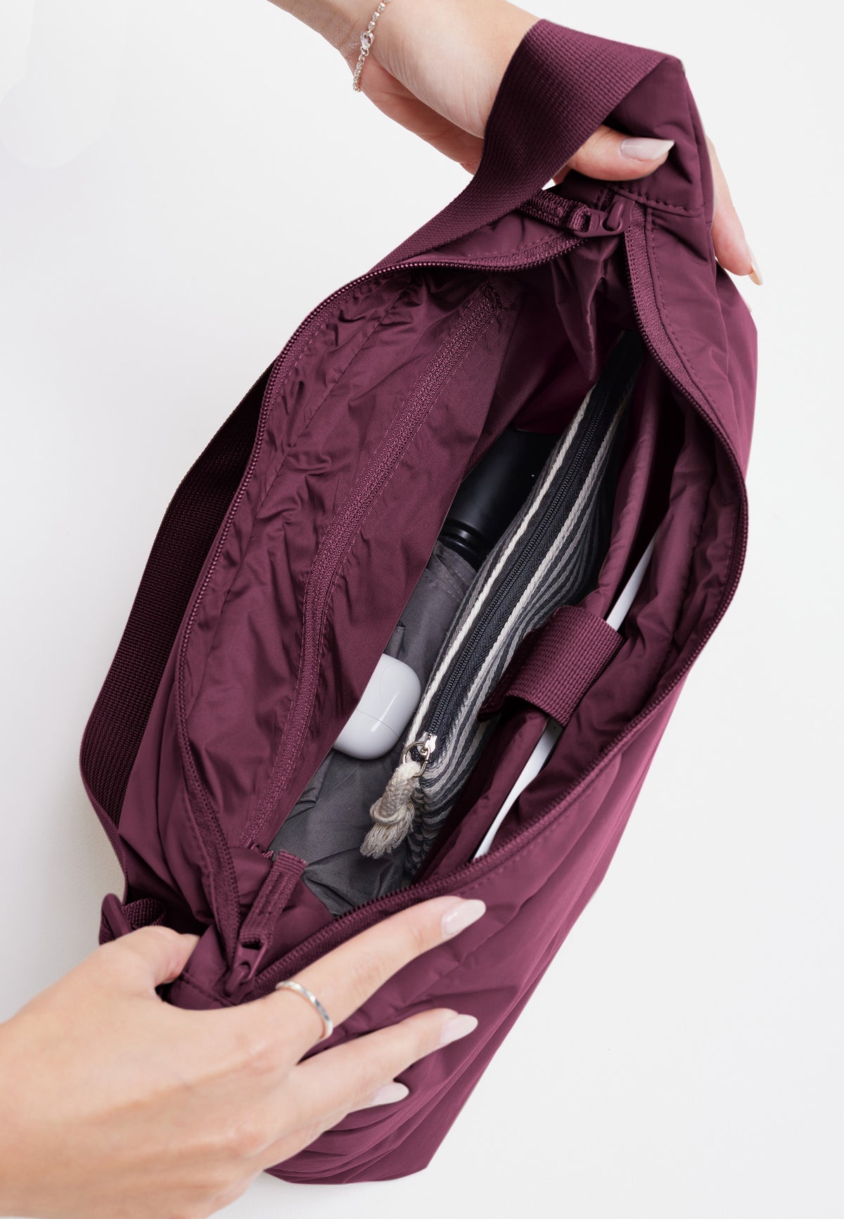 PUFFER SQUARE BAG Tasche in kraken (Weinrot) mit Blick ins geöffnete Innere, von Händen gehalten.