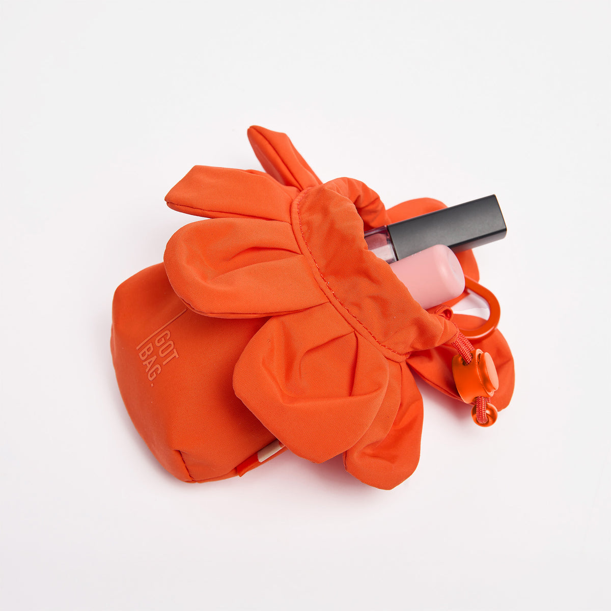 CHARM ANEMONE Tasche als Studioaufnahme, teilweise geöffnet mit Beauty-Produkten darin.