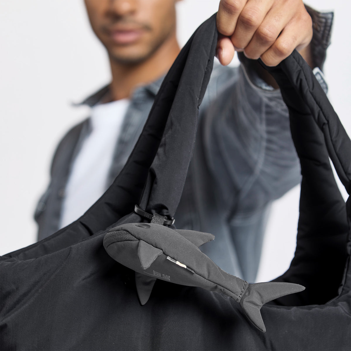 CHARM SHARK Accessoires an einer Tasche, von einem Mann in der Hand gehalten.