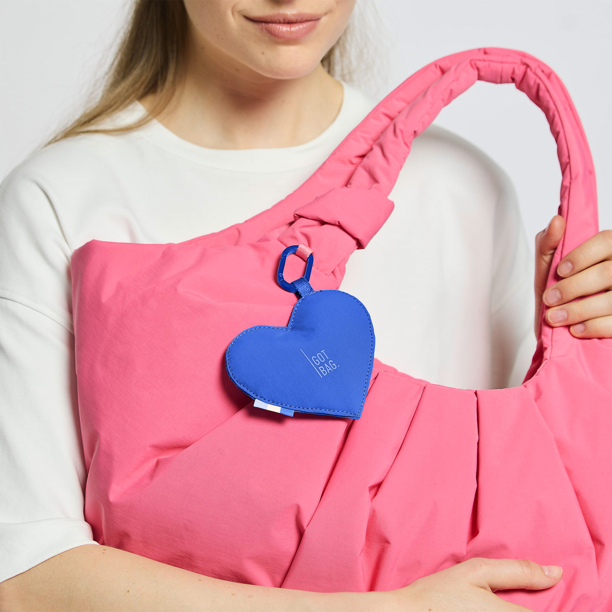 CHARM TREASURE Tasche mit blauem Herz-Anhänger, von einer Frau mit beiden Händen gehalten.
