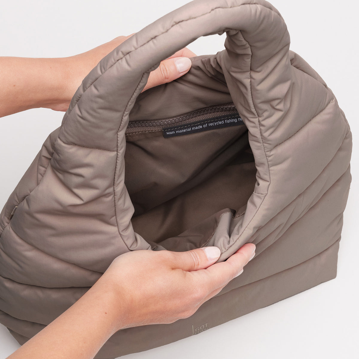 WAVY PUFFER SHOULDER BAG Tasche in oyster (klassisches Taupe-Braun), Hände halten sie offen.