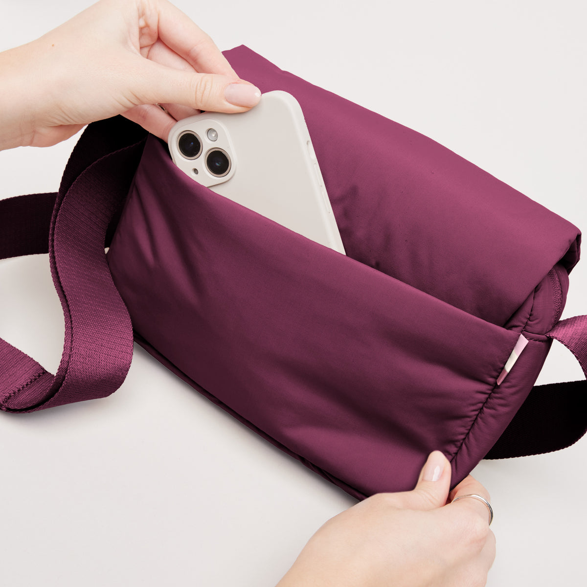 CLOUD CROSSBODY BAG Tasche in kraken (Weinrot) von einer Frau, die ein Smartphone in die Tasche legt.