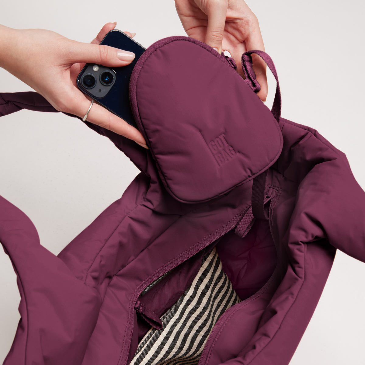 CLOUD TOTE BAG Tasche in kraken (Weinrot) mit Händen, die ein Smartphone in die Innentasche stecken.