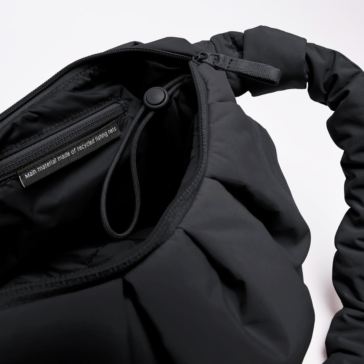 PLEAT MOON BAG LARGE Tasche in black (Schwarz) als Detailaufnahme des Innenraums mit Etikett zu recycelten Fischernetzen.