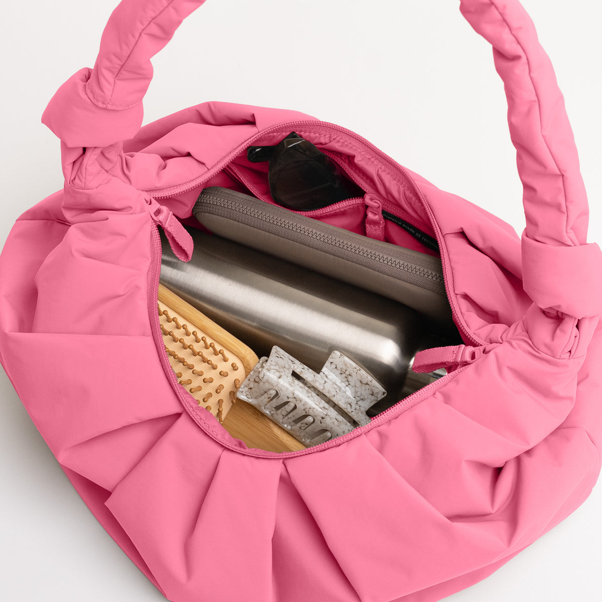 PLEAT MOON BAG LARGE Tasche in salina pink (leuchtendes Pink) als Draufsicht, geöffnet mit Inhalt.