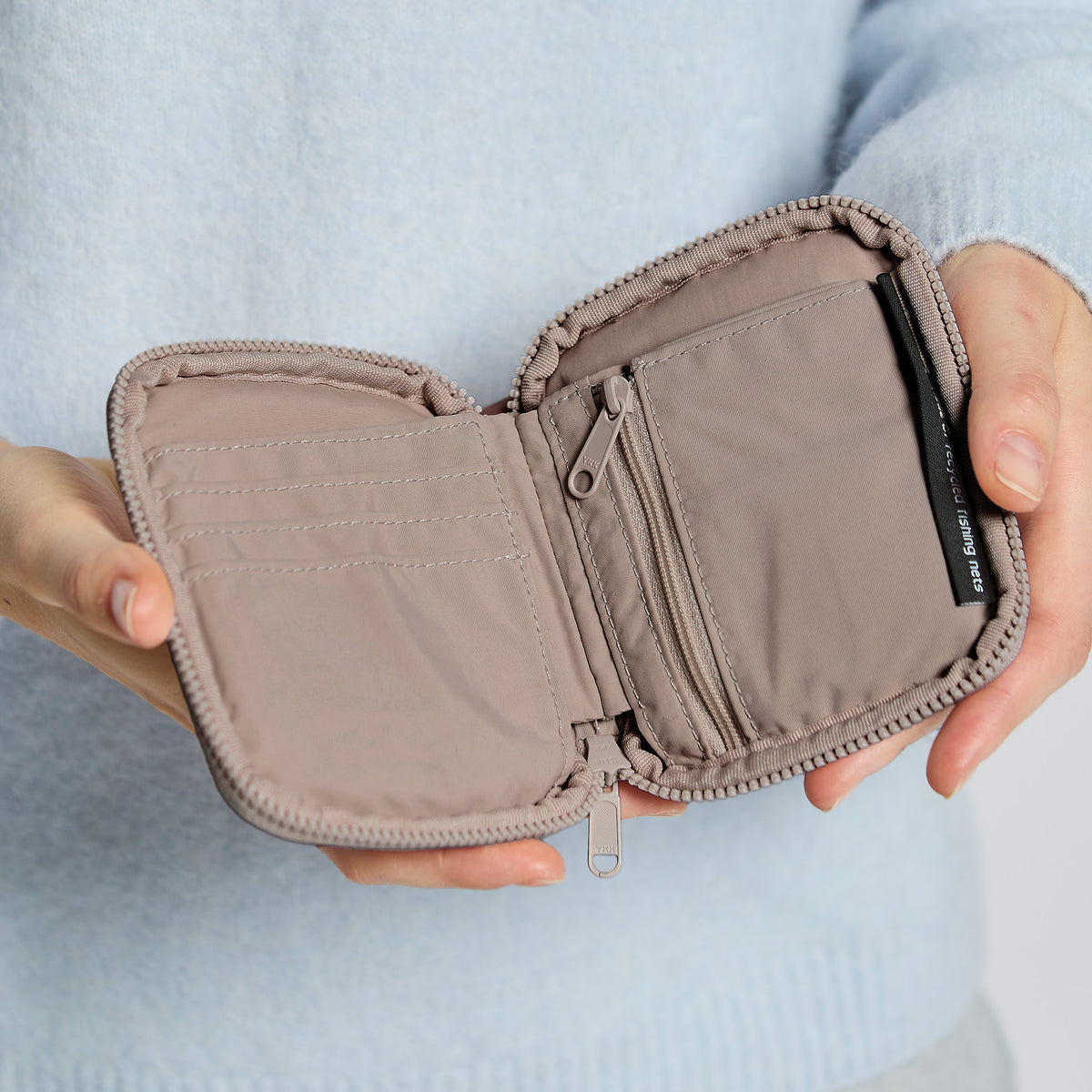 WALLET Accessoire in oyster (klassisches Taupe-Braun) von einer Frau in den Händen gehalten.