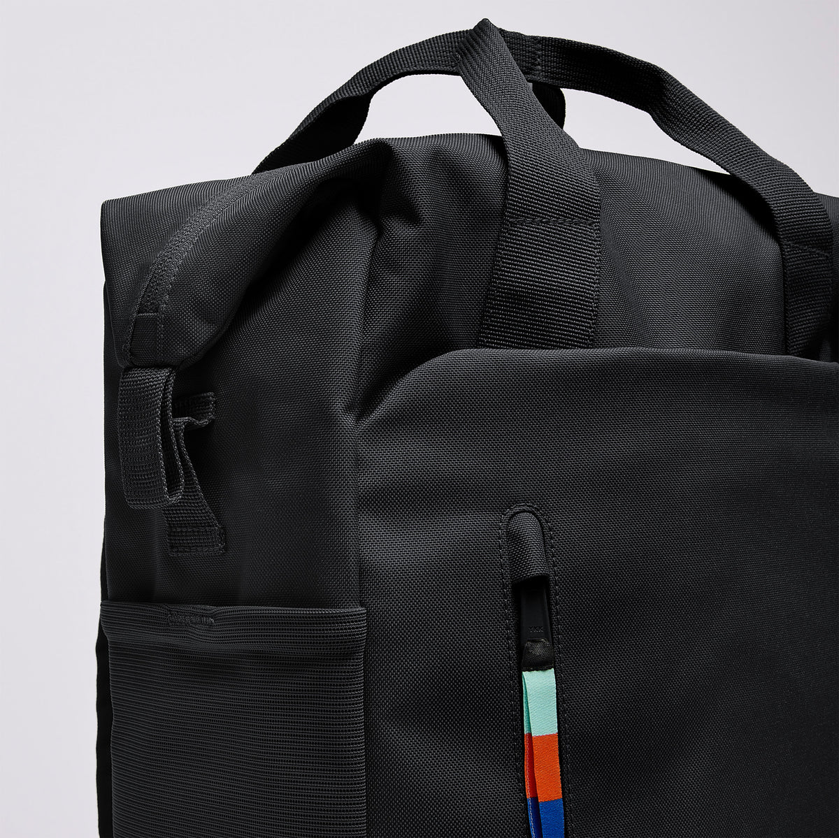 FLOW PACK Rucksack in black (Schwarz) in Detailansicht, zeigt Tragegriffe und Reißverschluss mit buntem Zipper-Puller.