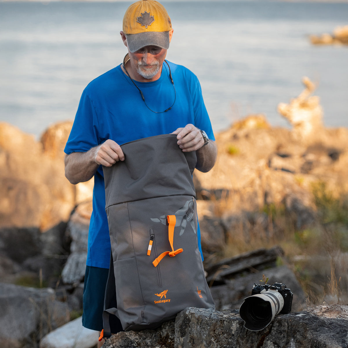 Ein Mann inspiziert seinen ROLLTOP EASY Rucksack am felsigen Ufer.