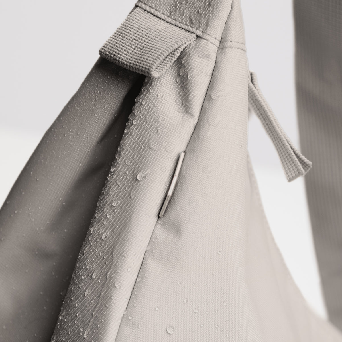 Detailaufnahme der MOON BAG LARGE Tasche in clam (helles, warmes Grau) mit Wassertropfen auf dem Stoff.