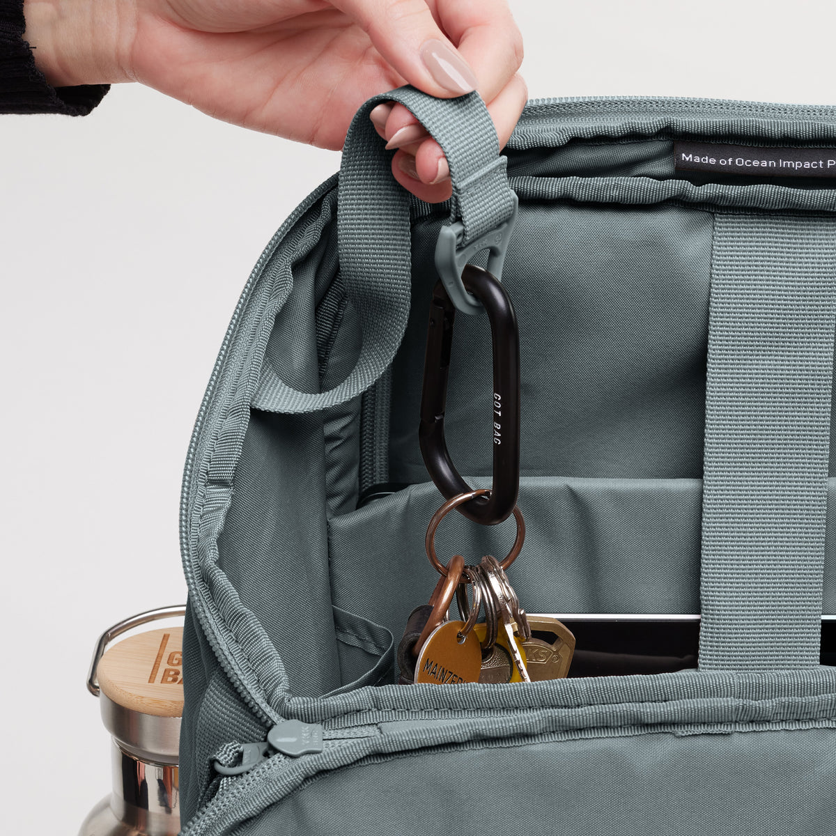 PRO PACK Rucksack in basalt (graues Eisblau). Detailaufnahme: Hand steckt Schlüssel in das Innere des Rucksacks.