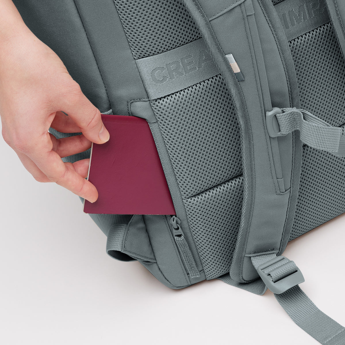 PRO PACK Rucksack in basalt (graues Eisblau), eine Hand steckt einen Reisepass in eine Geheimtasche.