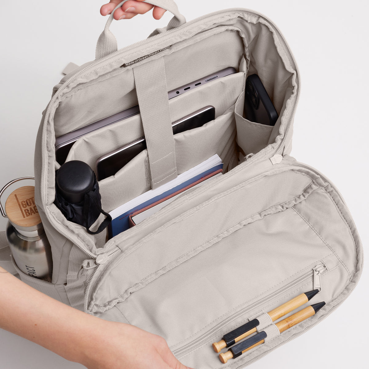 PRO PACK Rucksack in clam (helles, warmes Grau) offen, von Hand gehalten, zeigt Inneneinteilung. Hergestellt aus Ocean Impact Plastic.