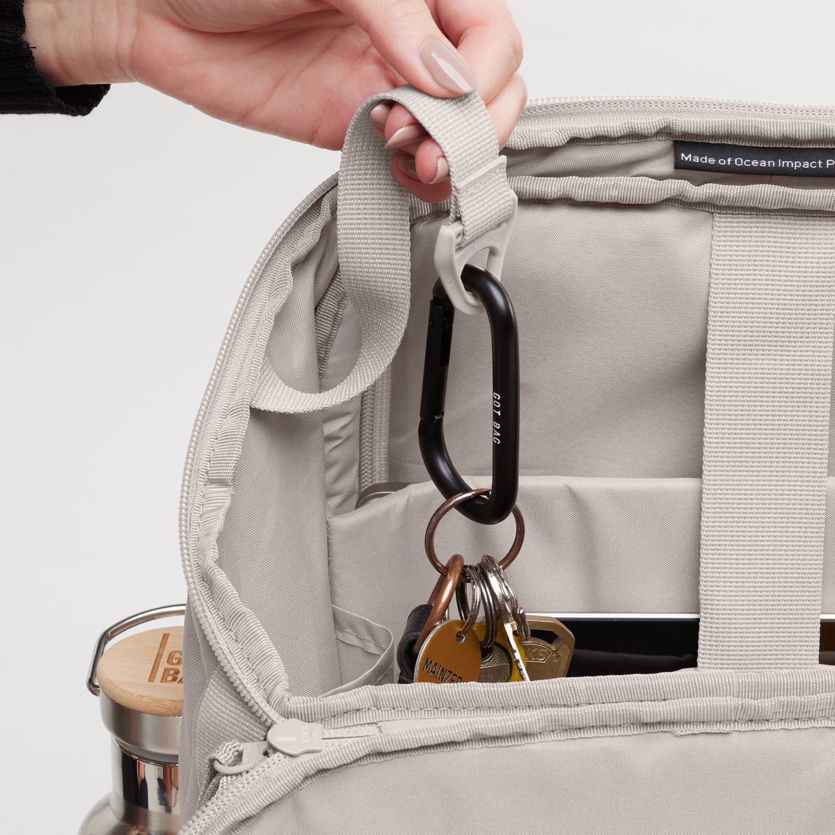 PRO PACK Rucksack in clam (helles, warmes Grau), eine Hand hält einen Schlüsselbund am Karabinerhaken.