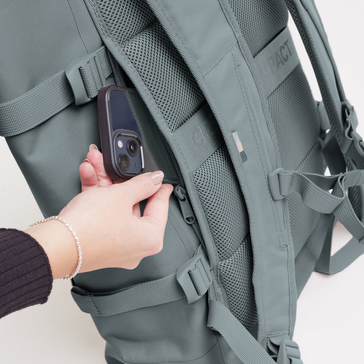 ROLLTOP 2.0 Monochrome Edition Rucksack in basalt (graues Eisblau), Smartphone wird von Frau aus der Geheimtasche genommen.