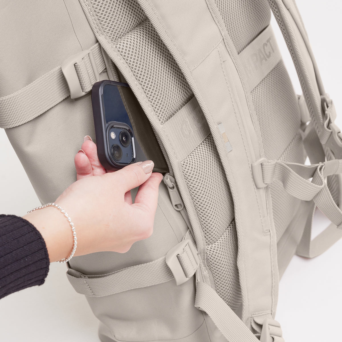 ROLLTOP 2.0 MONOCHROME EDITION Rucksack in clam (helles, warmes Grau), eine Frau öffnet eine Reißverschlusstasche am Rücken.