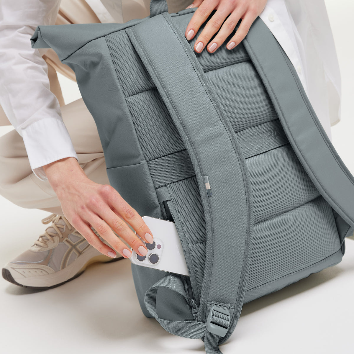 ROLLTOP EASY Rucksack in basalt (graues Eisblau), von einer Frau, die ein Smartphone in die Geheimtasche steckt.