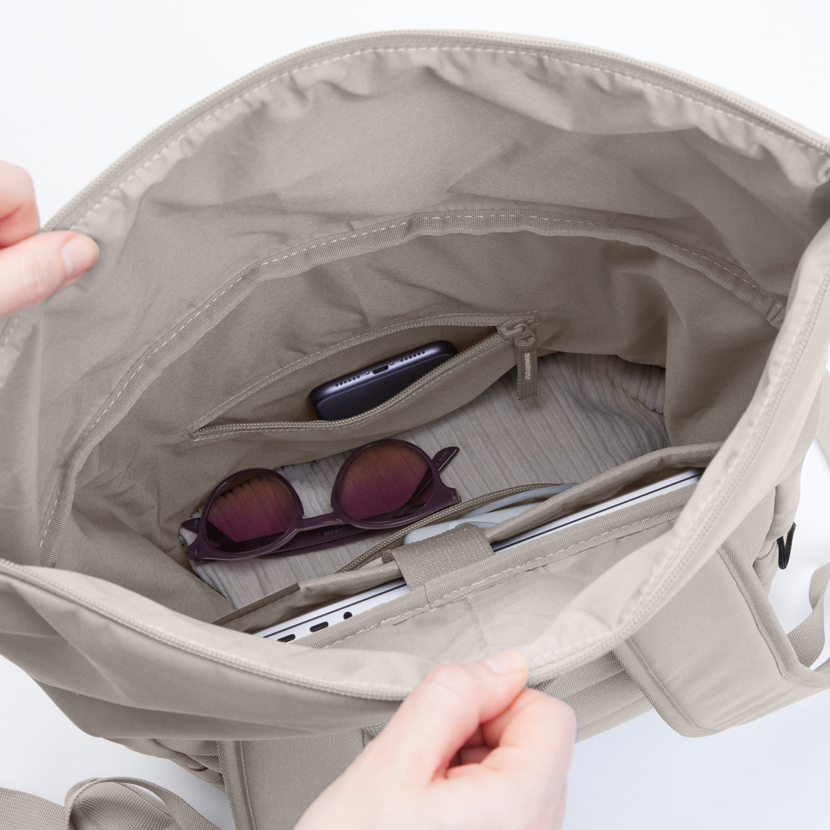 ROLLTOP EASY Monochrome Edition Rucksack in clam (helles, warmes Grau) mit Smartphone, Sonnenbrille und Laptop.