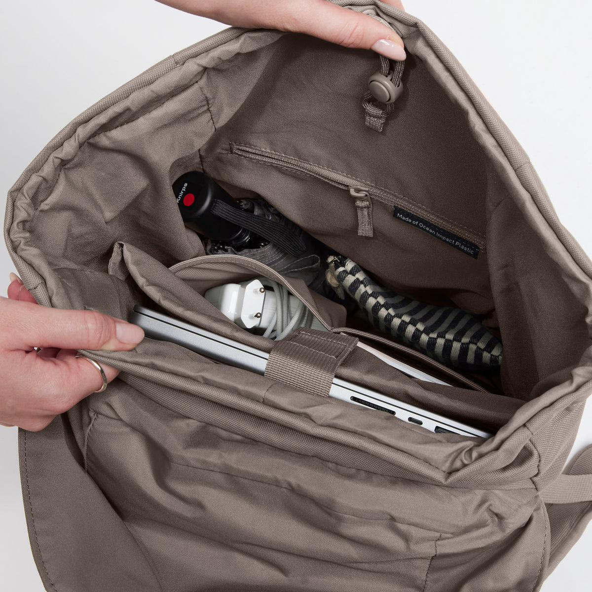 FLAP PACK Monochrome Edition Rucksack in oyster (klassisches Taupe-Braun), von einer Frau offen gehalten, zeigt Innenfach mit Laptop.