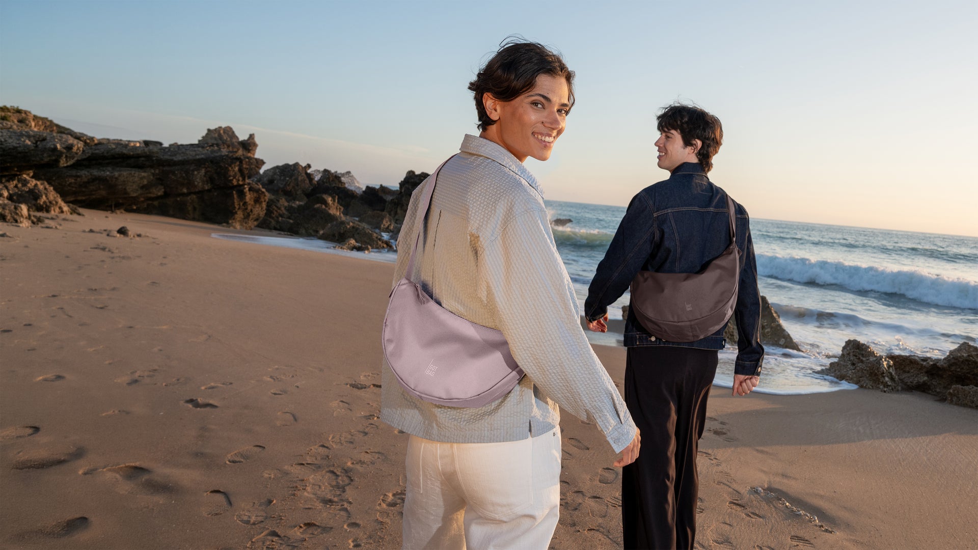 MOON BAG SMALL bag in pink dolphin () carried crossbody by a woman on the beach.