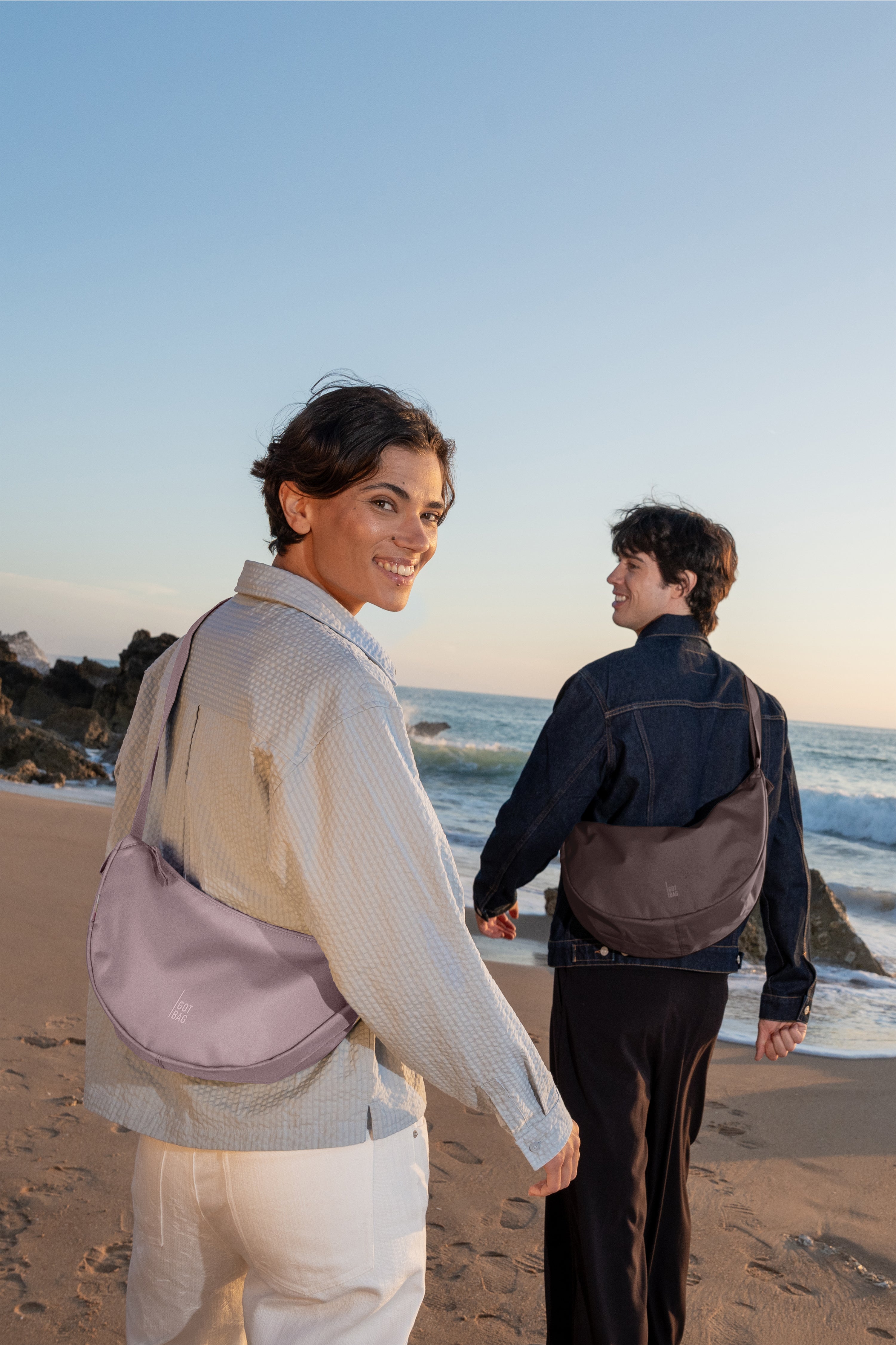 MOON BAG SMALL bag in pink dolphin () carried crossbody by a woman on the beach.