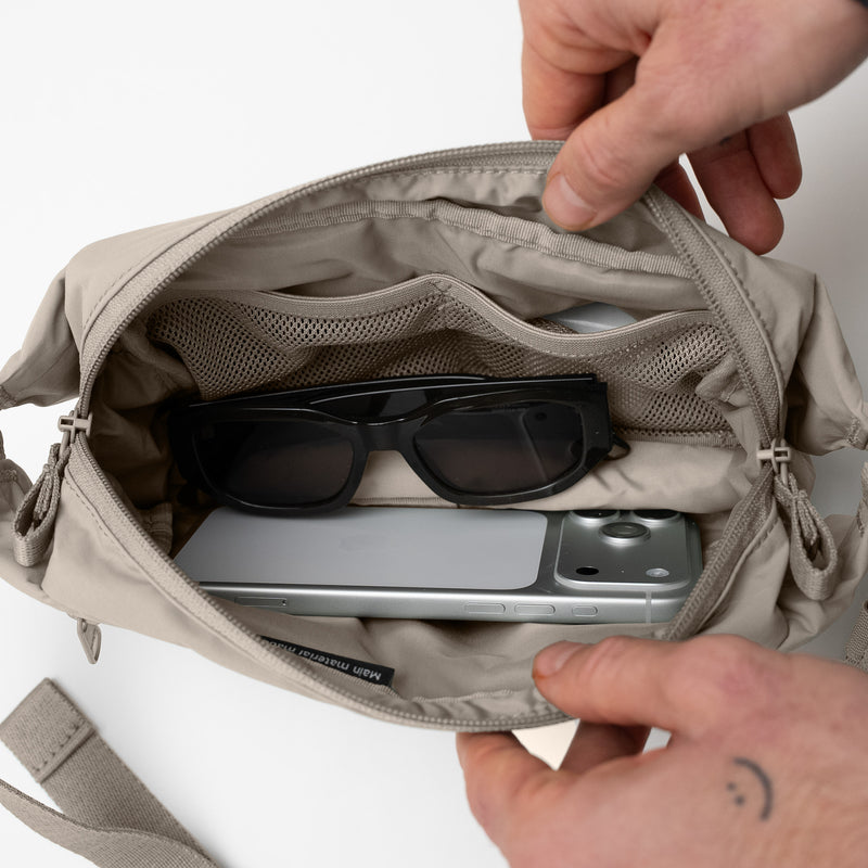 ADAPT SLING BAG Tasche in scallop (helles Beige) geöffnet, zeigt Innenfächer mit Handy und Sonnenbrille.