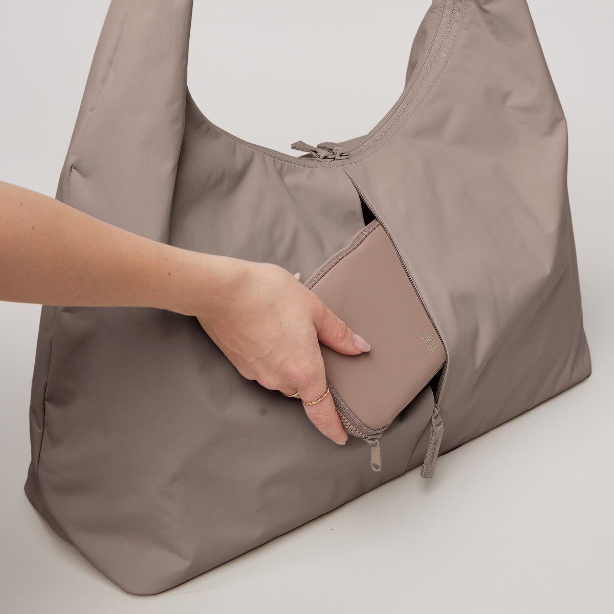 T SHAPE BAG LARGE Tasche in black (Schwarz) von einer Frau, die in die Reißverschluss-Rückentasche greift und eine Geldbörse hält.
