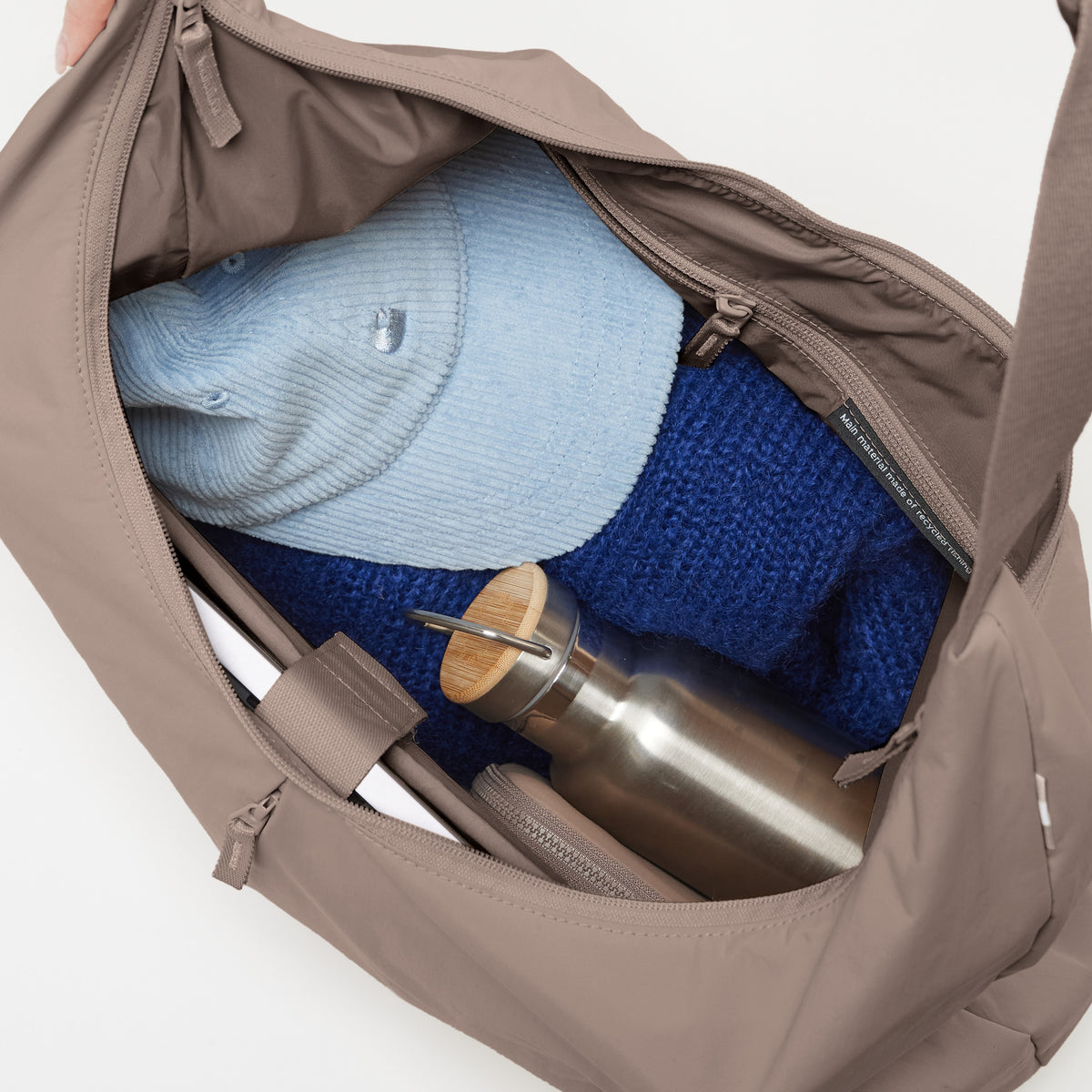 T-SHAPE BAG LARGE MONOCHROME EDITION Tasche in black (Schwarz), innen mit blauem Pullover, Mütze und Trinkflasche.