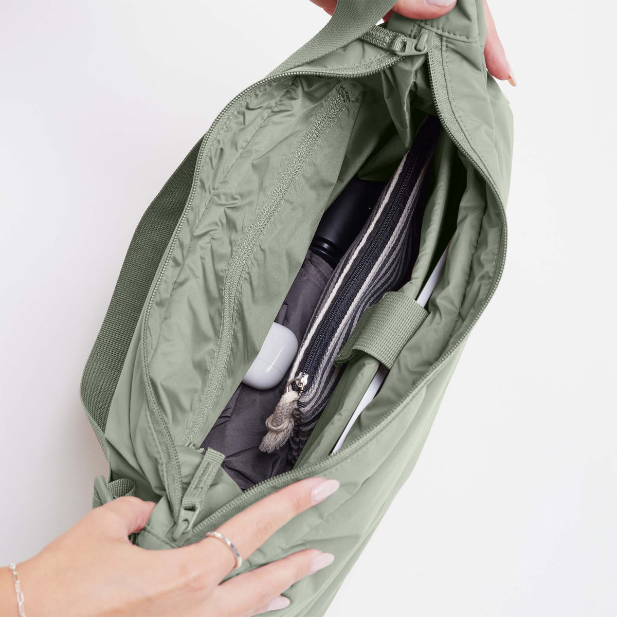 PUFFER SQUARE BAG Tasche in bass (Salbeigrün) von einer Frau offen gehalten, um den Inhalt zu zeigen.